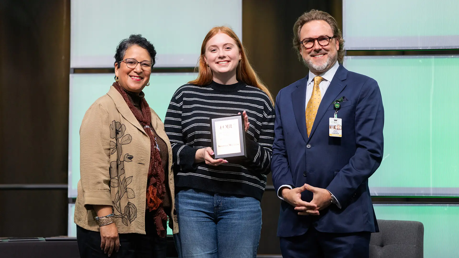 Dr. Lyda Murillo Wilbur, chair of the Division of Language and Literature, left, and OBU President Dr. Heath A. Thomas, right, presented the Outstanding Senior Award from the Division of Language and Literature to Savannah Mayfield, center.
